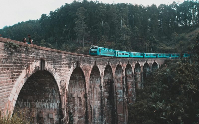 A blue train traverses the iconic Nine Arch Bridge in Ella, surrounded by lush Sri Lankan forests.