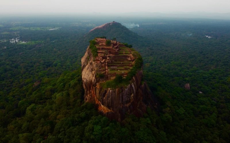A stunning aerial view of Sigiriya Rock Fortress rising above lush greenery in Sri Lanka.